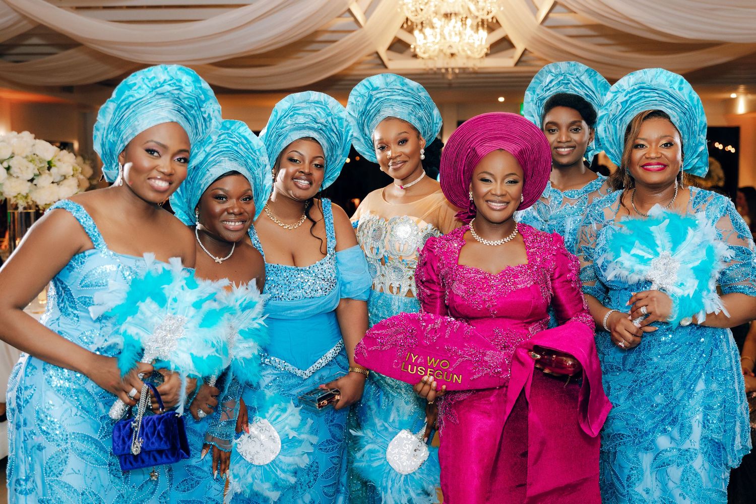 Wedding party wearing vibrant turquoise traditional African attire and pink dress poses together at reception venue.