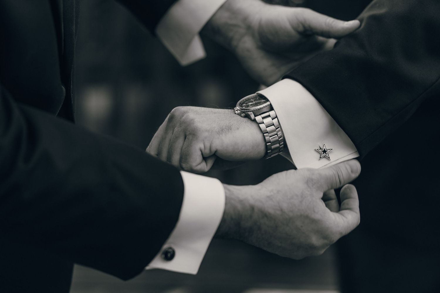 Close-up of hands adjusting formal watch and cufflinks in black and white.