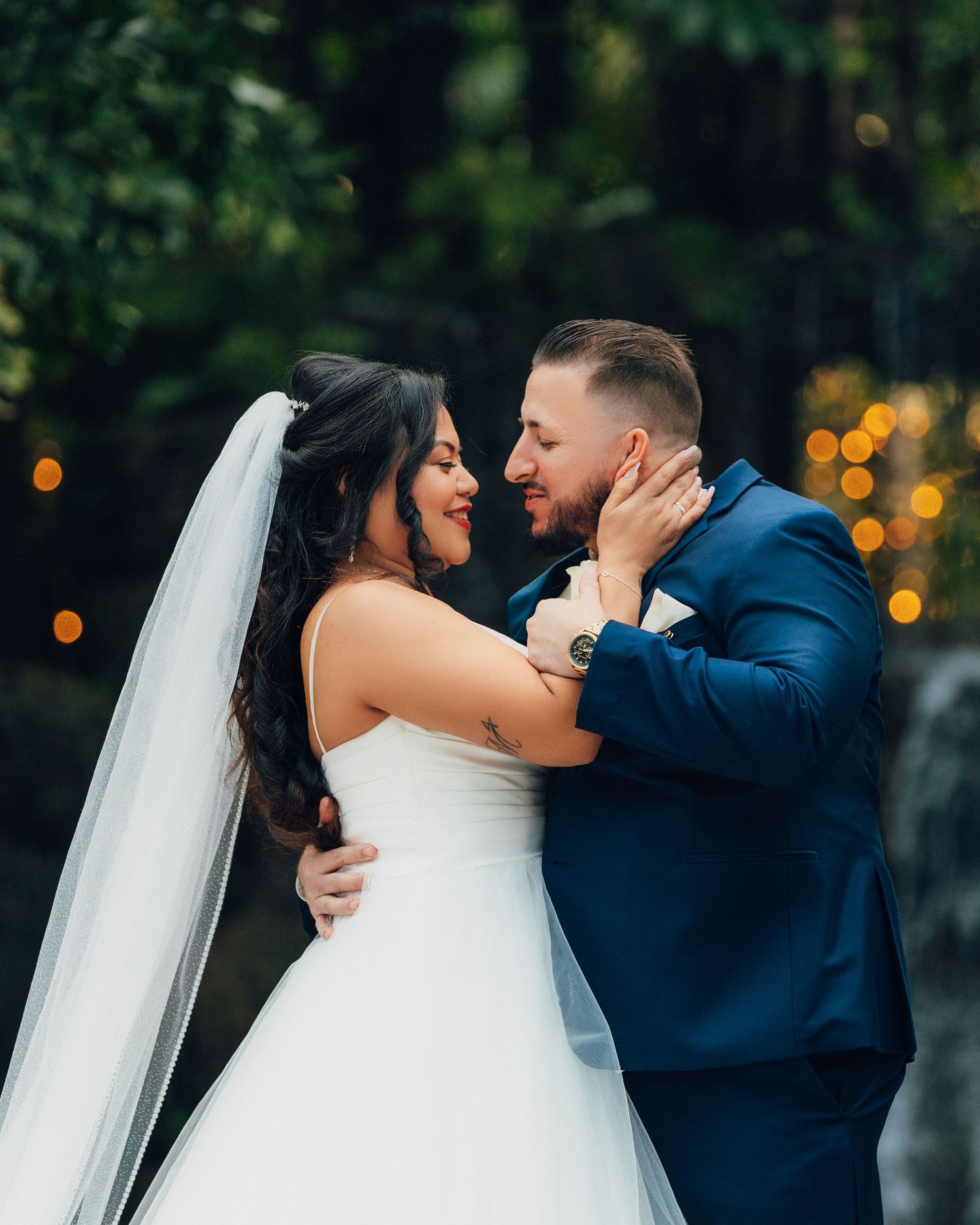 Romantic outdoor wedding portrait with couple embracing against evening bokeh lights.