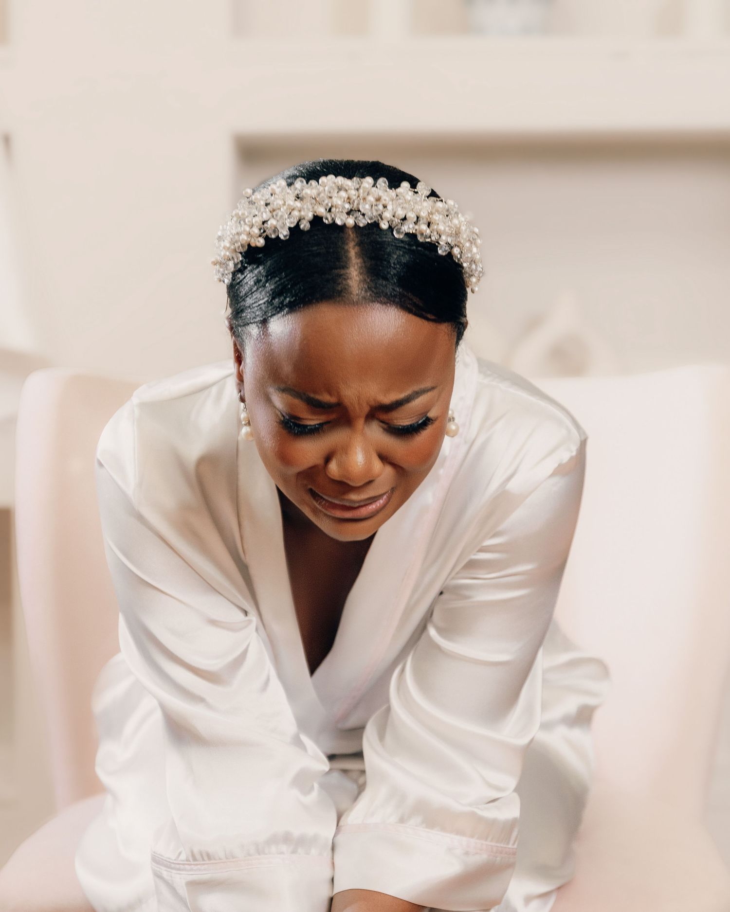 Candid moment showing a joyful laugh while wearing a delicate pearl headpiece and white silk robe.