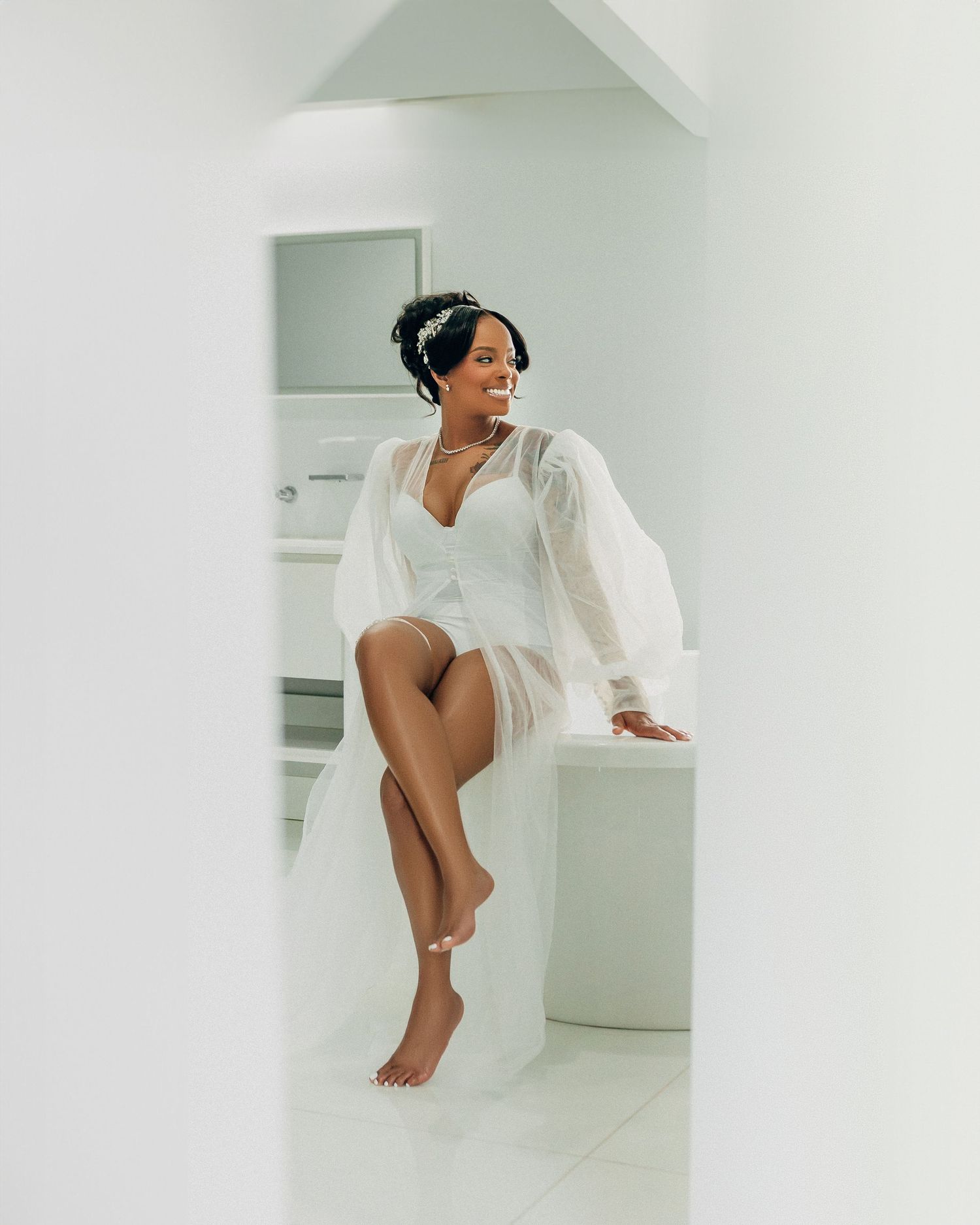 Modern bridal boudoir photo in minimalist white setting showing playful pose.