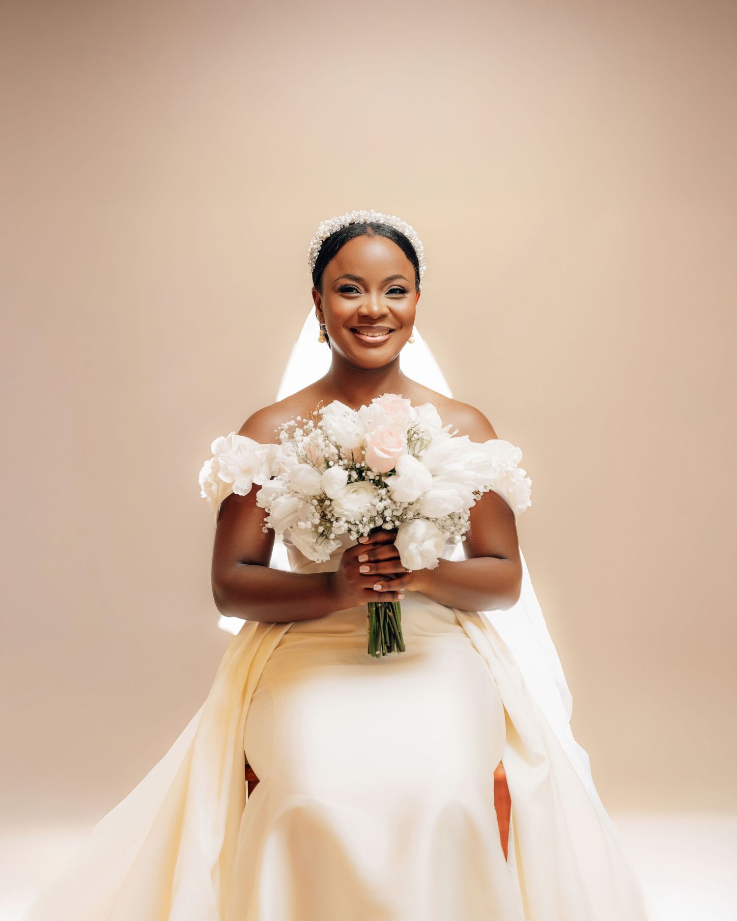 A radiant bride in an elegant white off-shoulder wedding gown holds a beautiful bouquet of white flowers.