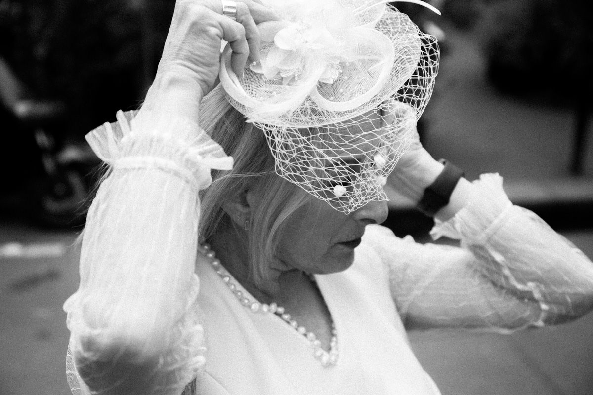 Black and white portrait of bride adjusting veil with delicate lace details.