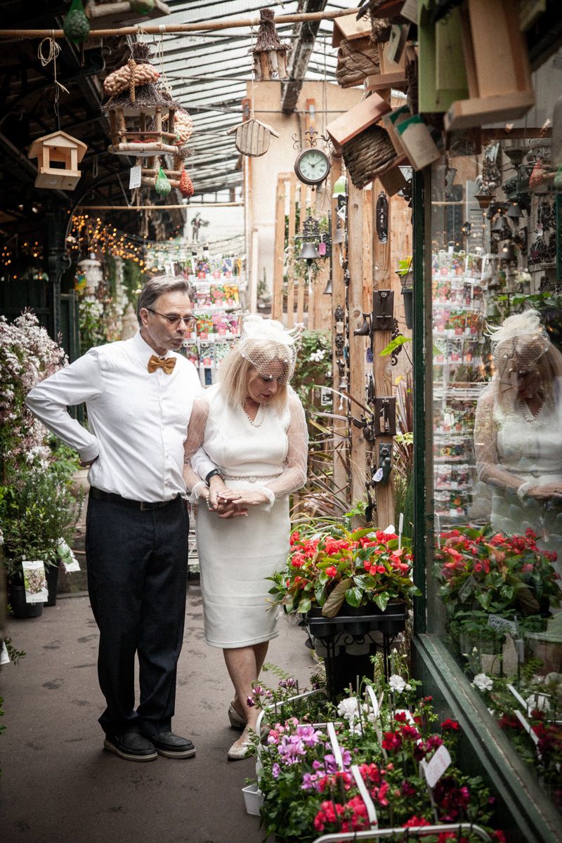 Couple browsing flower market with hanging birdhouses and garden decorations.