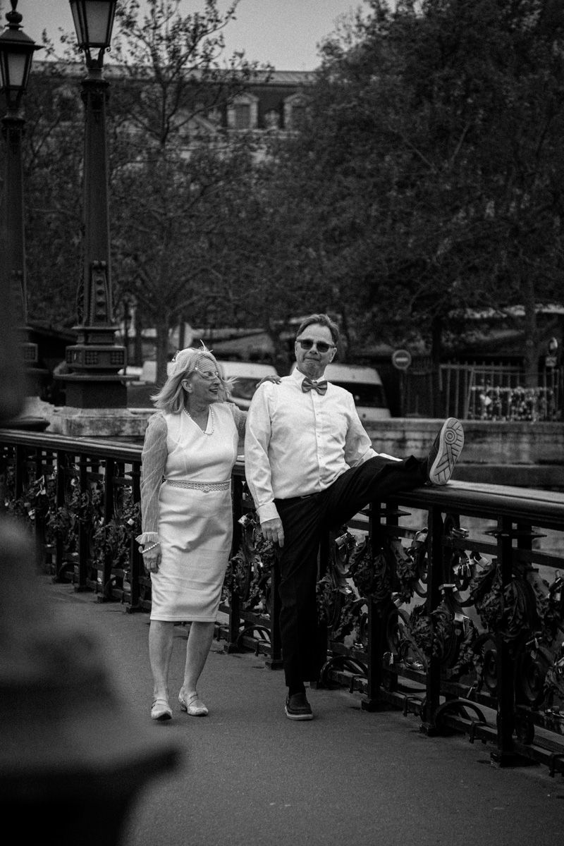Stylish couple posing on a bridge with ornate iron railings in black and white.
