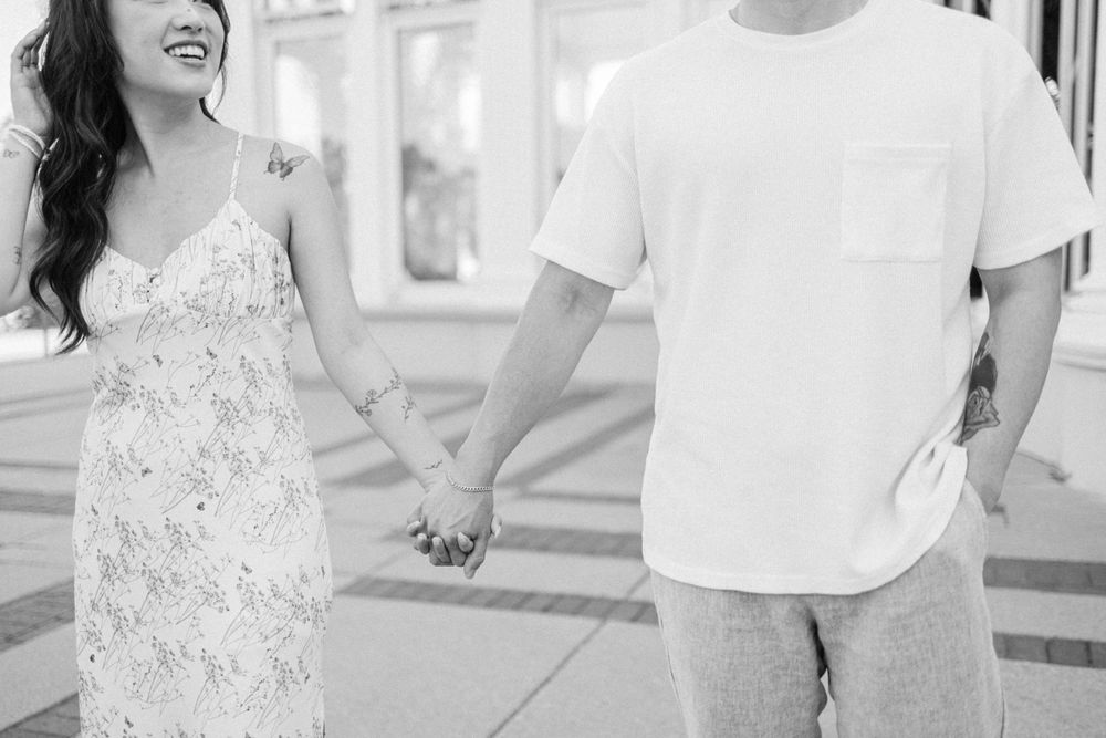 A couple holding hands in black and white, with she wearing a floral dress and he in casual attire.