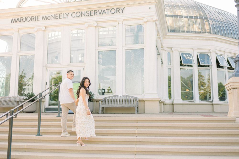 A couple poses on the steps of the Marjorie McNeely Conservatory in romantic engagement photos.