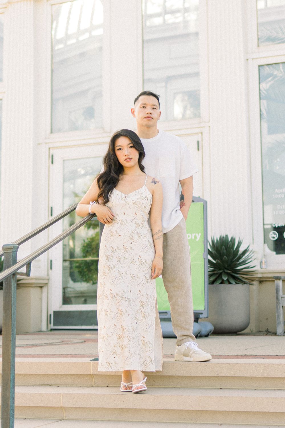 Couple in casual and formal wear pose on stone steps at a conservatory entrance.