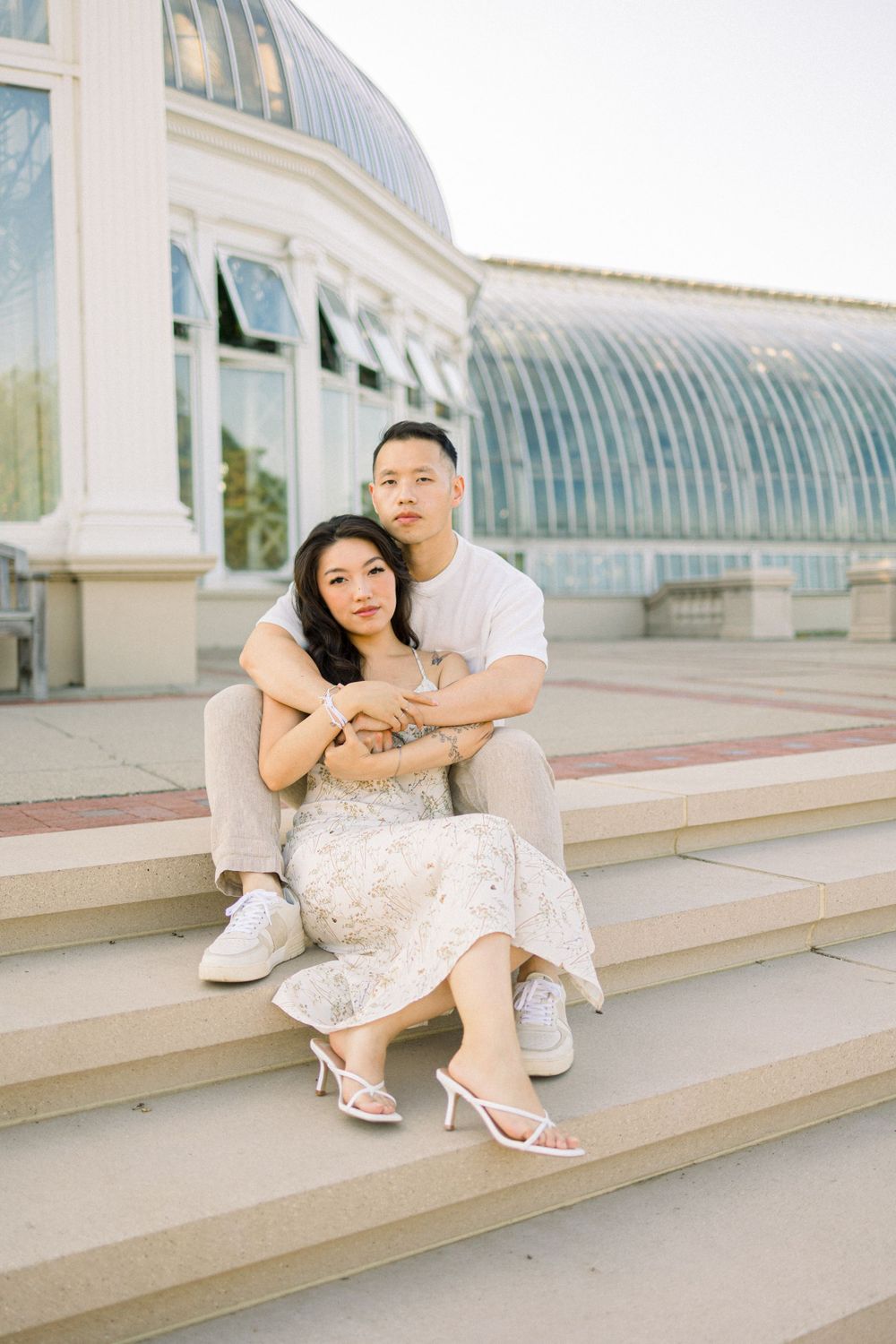 Intimate couple portrait on conservatory steps with glass dome architecture in background.
