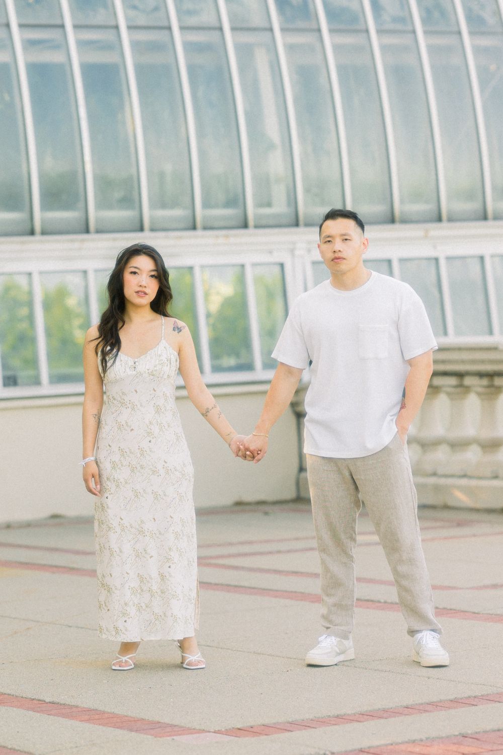 Couple holding hands in front of curved glass conservatory architecture.