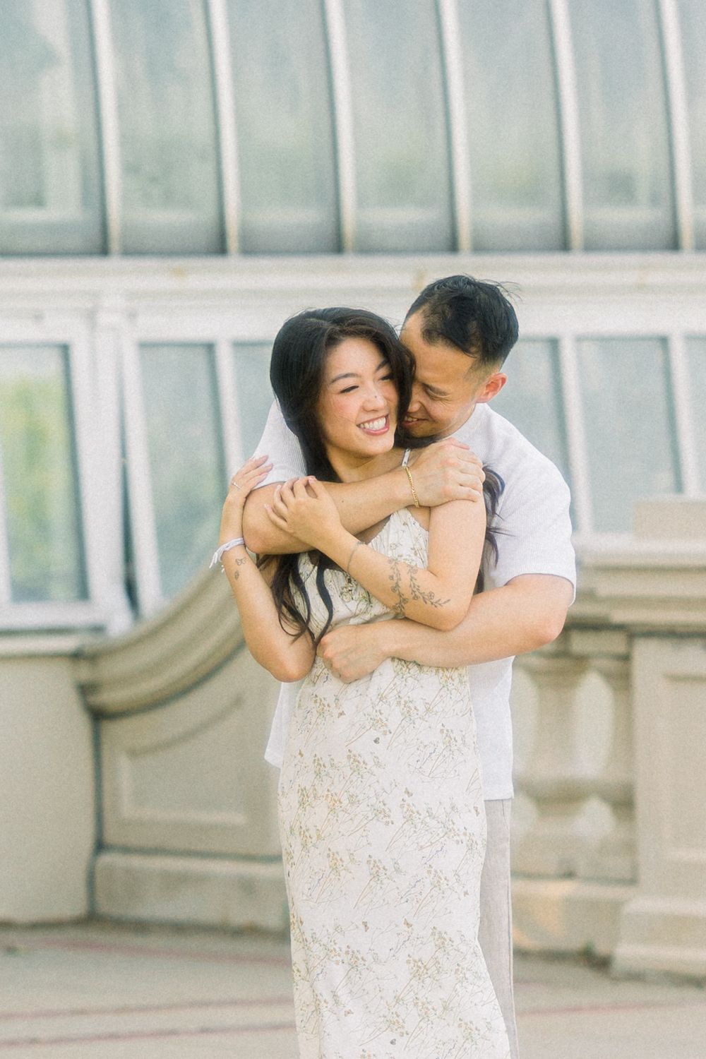 Romantic embrace captured in front of glass conservatory windows.
