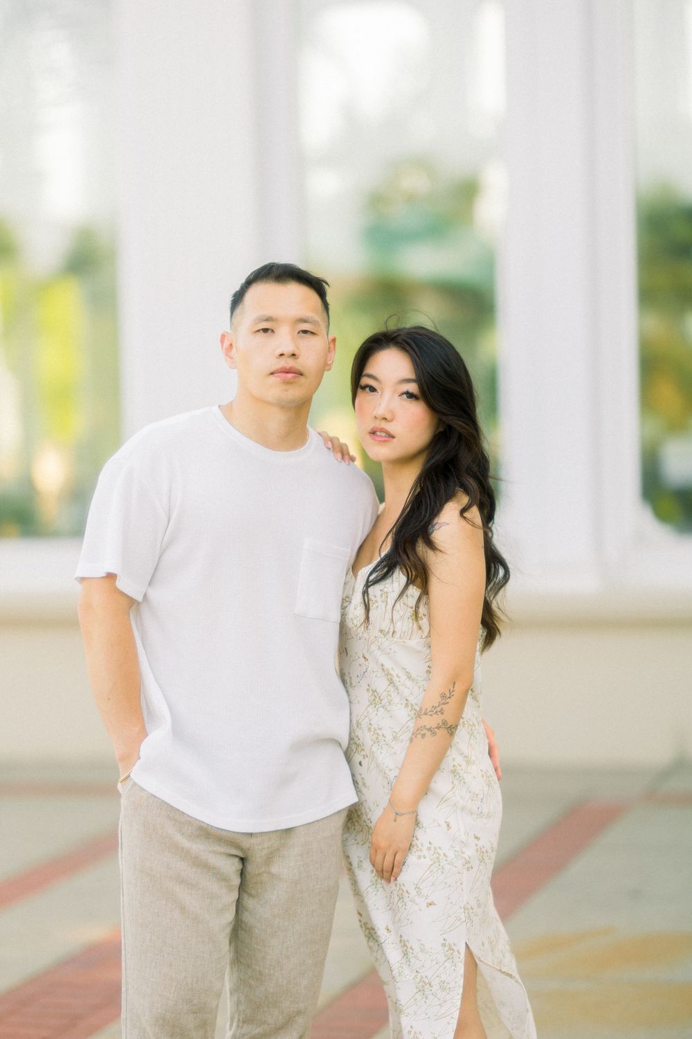 Stylish couple strikes elegant pose against conservatory backdrop.