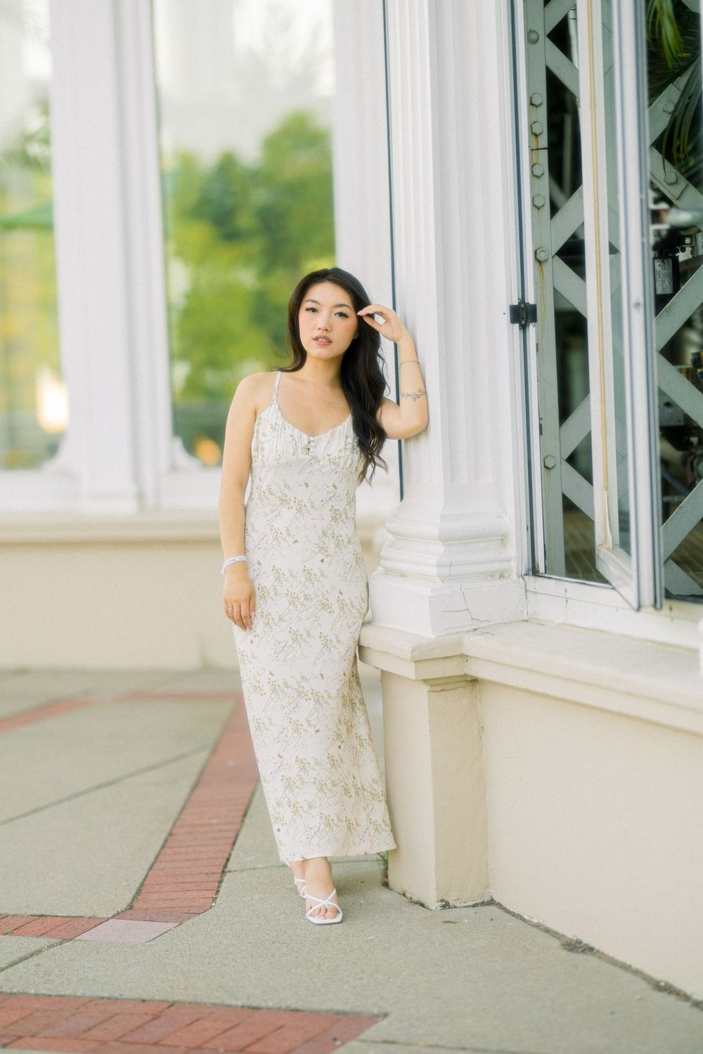 A woman in a delicate white lace dress poses elegantly against a white architectural backdrop.