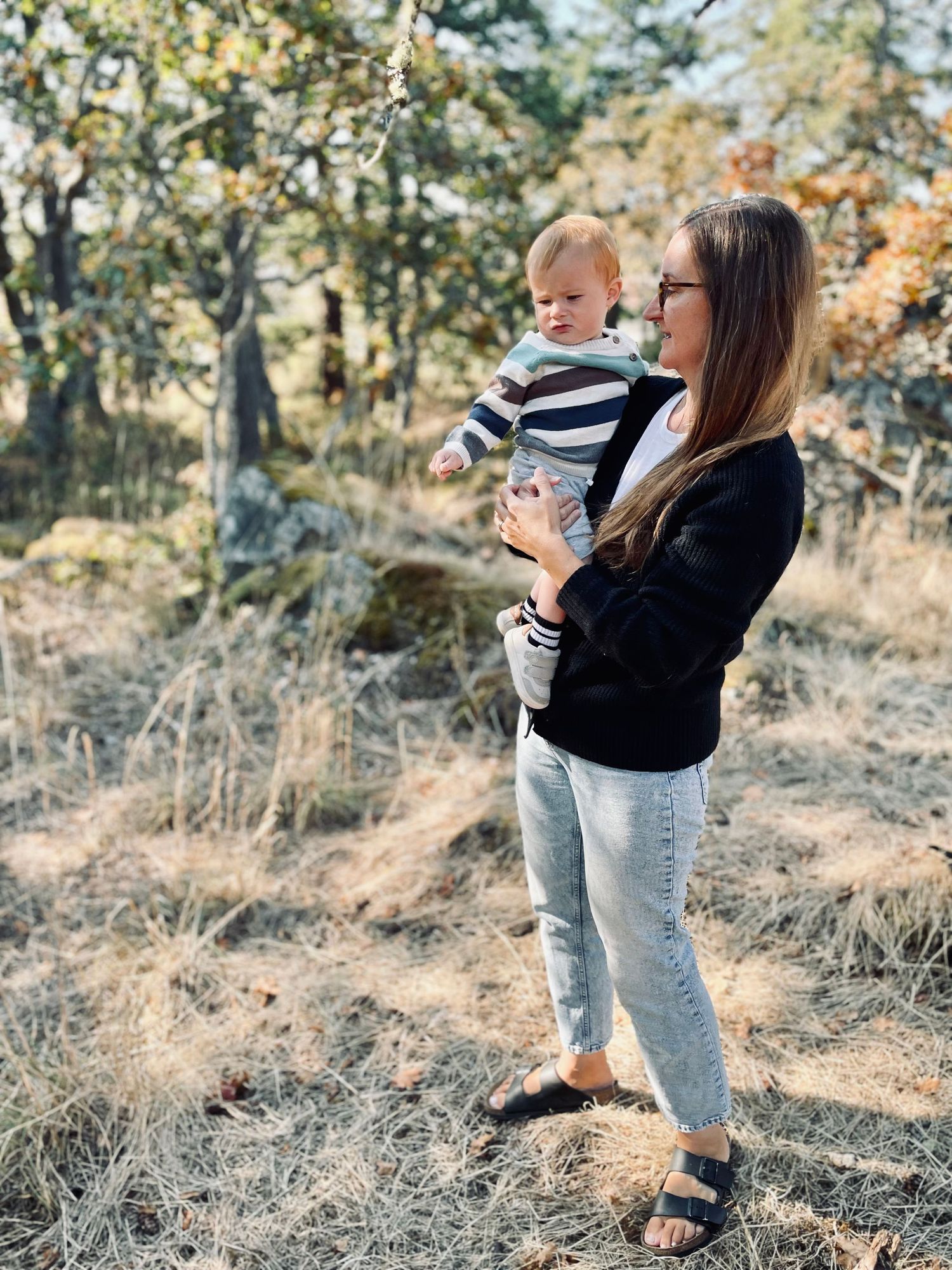 Mother and toddler explore autumn woods together in casual wear against natural forest backdrop.