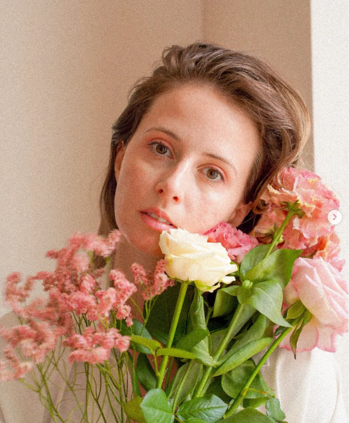 Grainy warm self-portrait of a girl holding pink flowers