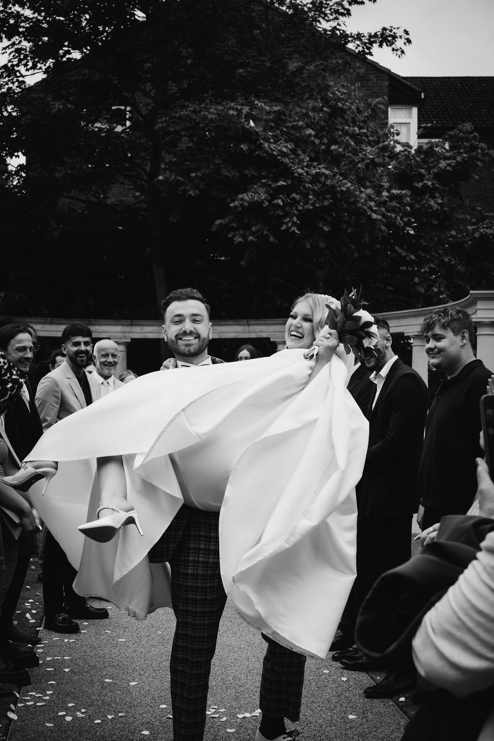 A joyful wedding moment captured in black and white as a couple celebrates with guests outdoors.