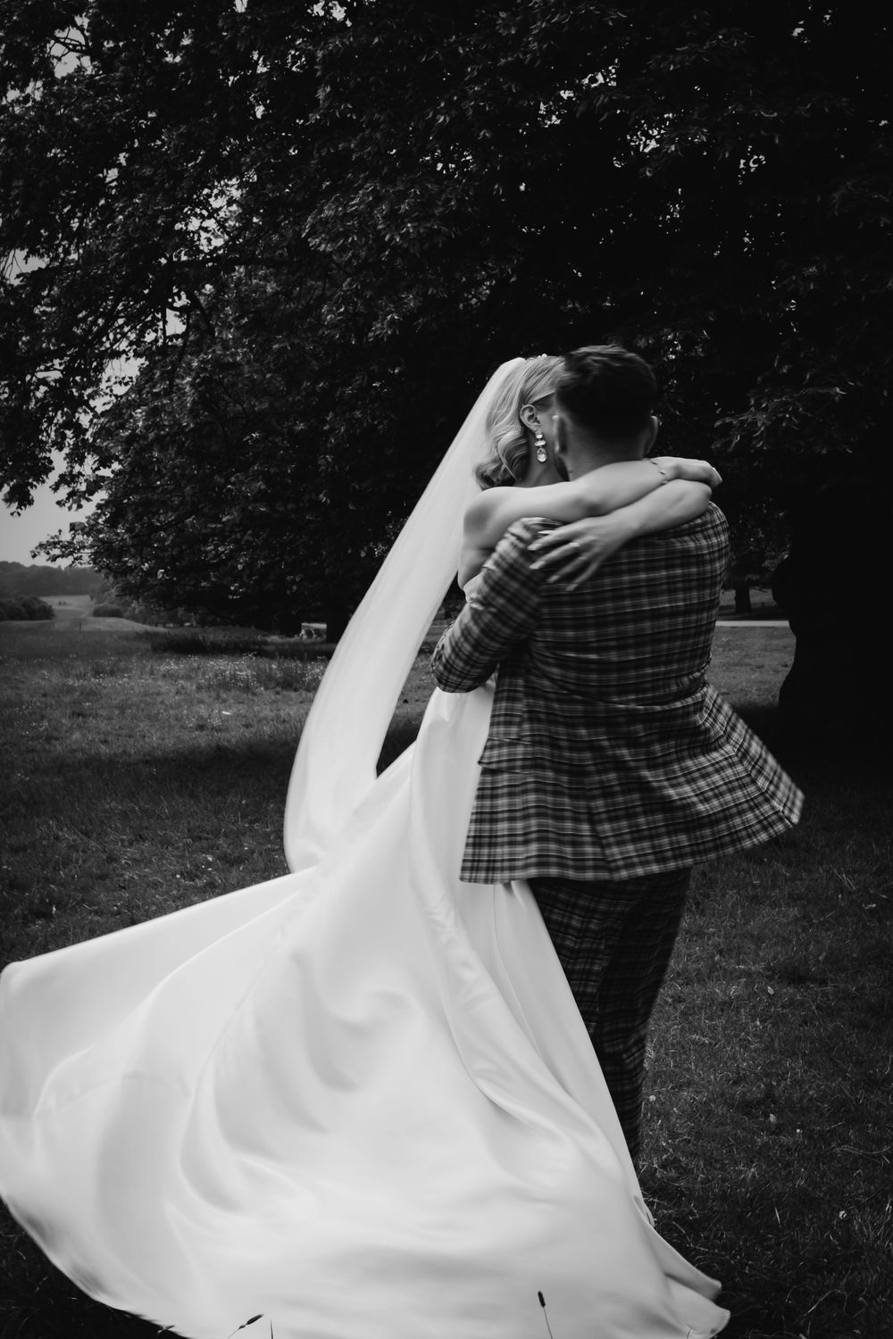 A romantic black and white wedding photo showing an intimate embrace with the bride's flowing white dress in motion.
