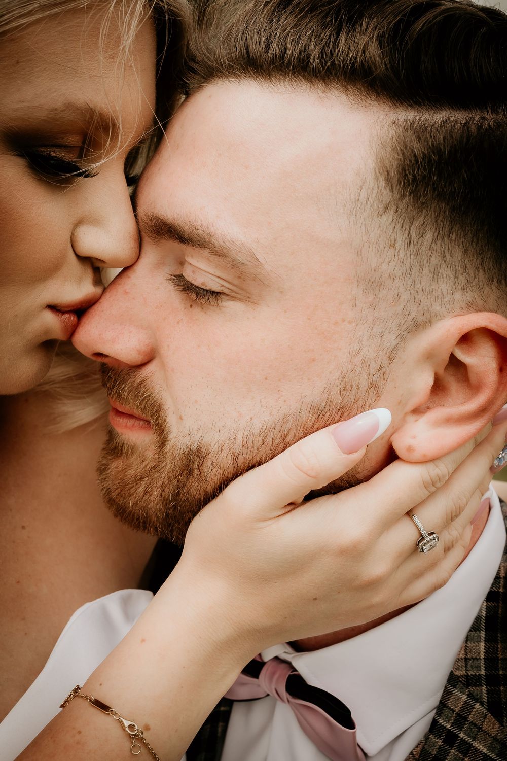 Close up romantic portrait of two people sharing an intimate moment with her hand on his face showcasing an engagement ring.