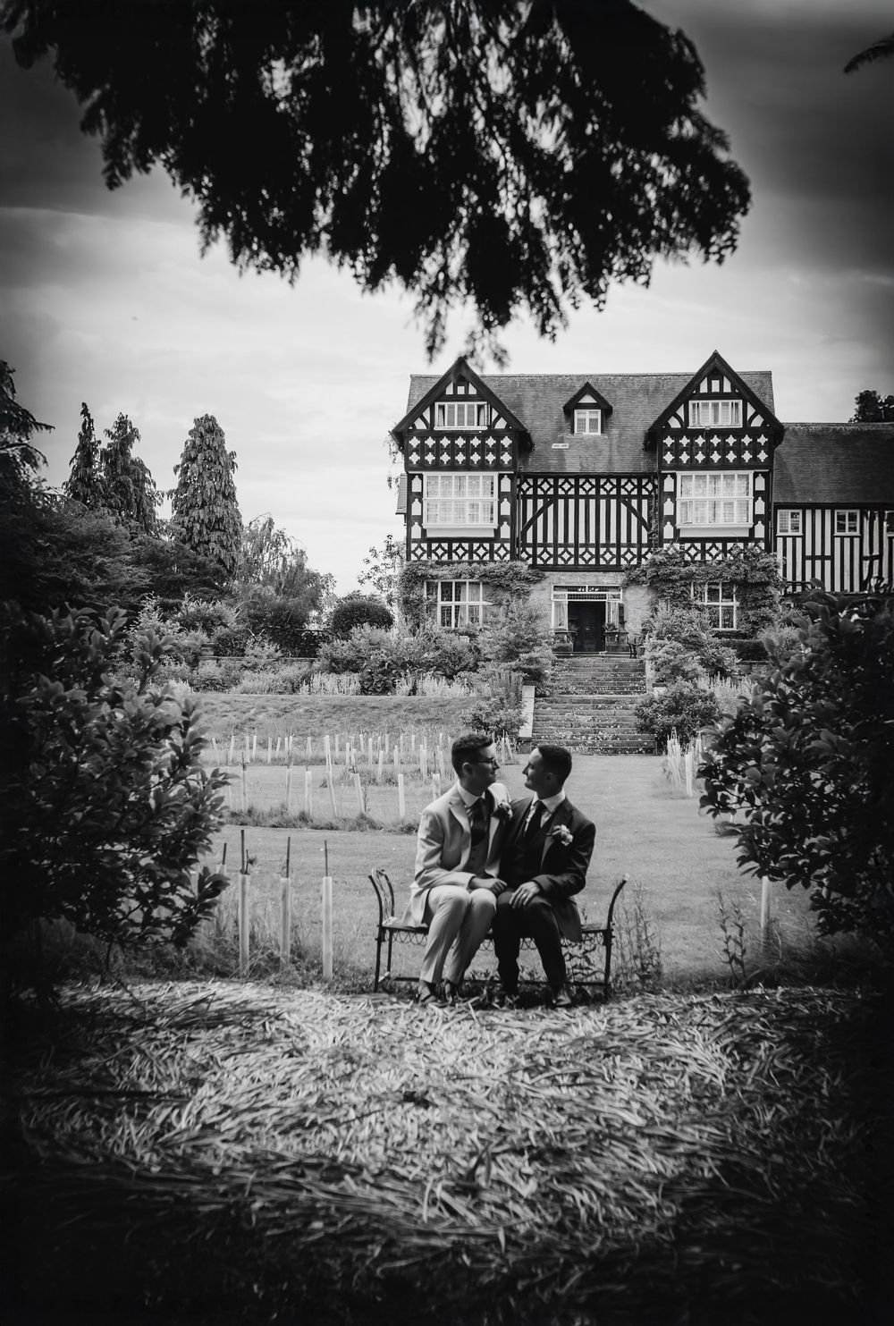 A black and white photo series showing silhouetted figures sitting on a garden bench with a tudor-style house in the background.