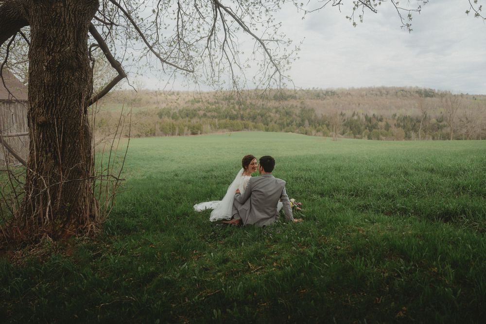 A couple shares a peaceful moment sitting together under a tree in a meadow.