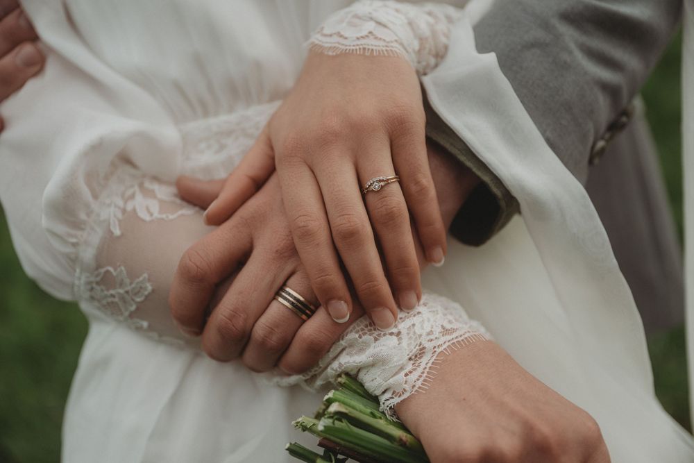Delicate lace sleeve detail with hands holding a bouquet stem and showing wedding rings.