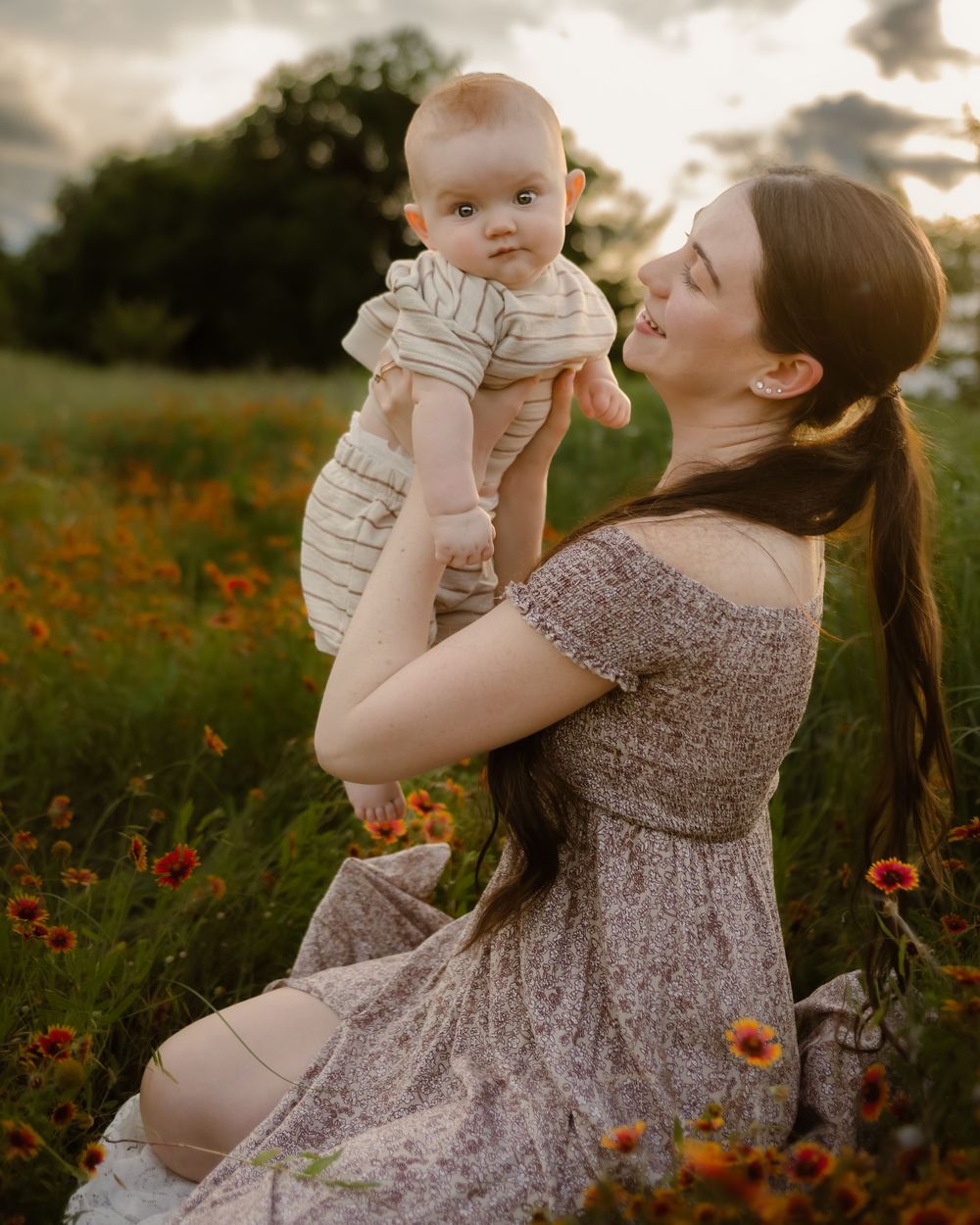A tender moment captured in a wildflower meadow at sunset as a baby is held up in a floral field.