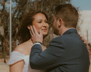 A tender moment captured between a couple on their wedding day, with warm sunlight filtering through trees in the background.