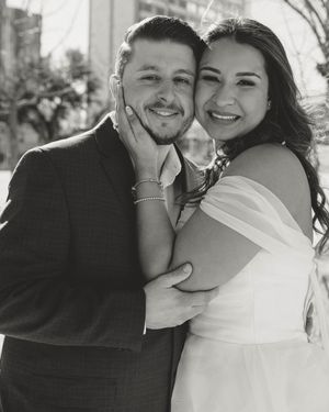 A black and white photo of a happy couple embracing on their wedding day, with the bride in a white off-shoulder dress.
