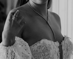A delicate white lace wedding dress bodice with off-shoulder detail and a thin silver necklace shown in black and white.