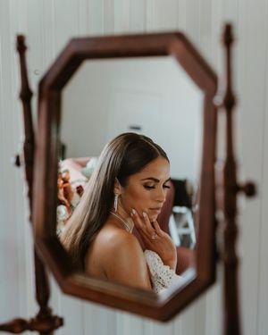 A reflection in an octagonal wooden mirror shows a bride in a lace wedding dress touching her neck thoughtfully.