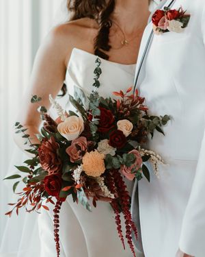 Wedding bouquets featuring burgundy and blush roses with cascading greenery arranged in a row.