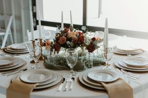 Elegant wedding table setting with white plates, candles and floral centerpiece in warm autumn colors.