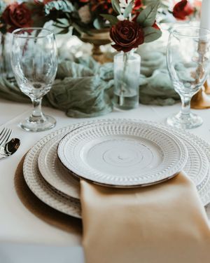 Elegant table setting with white embossed plates, crystal wine glasses, and a red rose centerpiece on a white tablecloth.