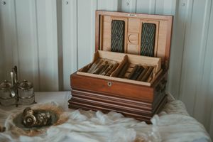Vintage wooden cigar humidor display case with leather accents and brass decorative elements shown open on white surface.
