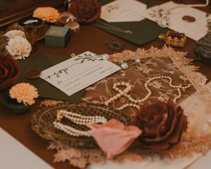 Vintage wedding accessories including roses, pearls, lace, and paper ephemera arranged on a wooden table.
