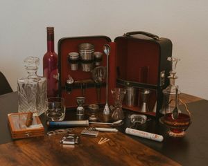 Vintage travel bar set with red case, glass decanters, and bar tools arranged on wooden table.