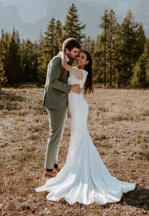 Romantic wedding embrace photographed in mountain meadow during golden hour.