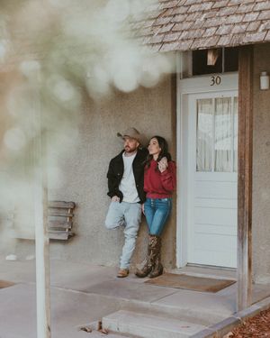 A couple stands together on a rustic porch with bokeh lighting, wearing casual attire outside house number 30.