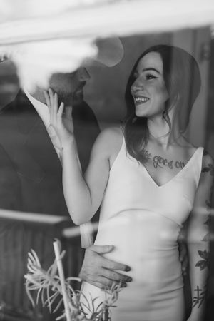 An intimate black and white portrait of a couple sharing a joyful moment indoors, with the woman wearing a white dress.