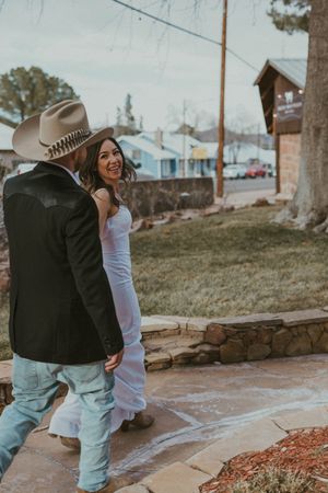 A couple in western attire share a candid moment on a stone path during an outdoor photoshoot.