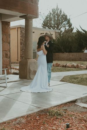 A couple sharing a romantic moment on a concrete patio with a stone column and landscaping in the background.