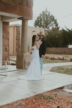 A couple shares a sweet moment on a porch with brick columns and autumn leaves scattered on the ground.