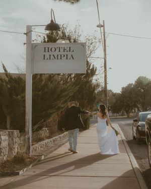A couple walks down a vintage hotel-lined street with vintage signage and palm trees in a muted retro style.