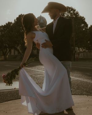 A romantic sunset portrait of a couple dancing, with the bride in a flowing white gown and cowboy hat-wearing groom.