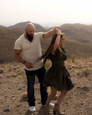 A couple dancing together in a desert landscape with mountains in the background during golden hour.