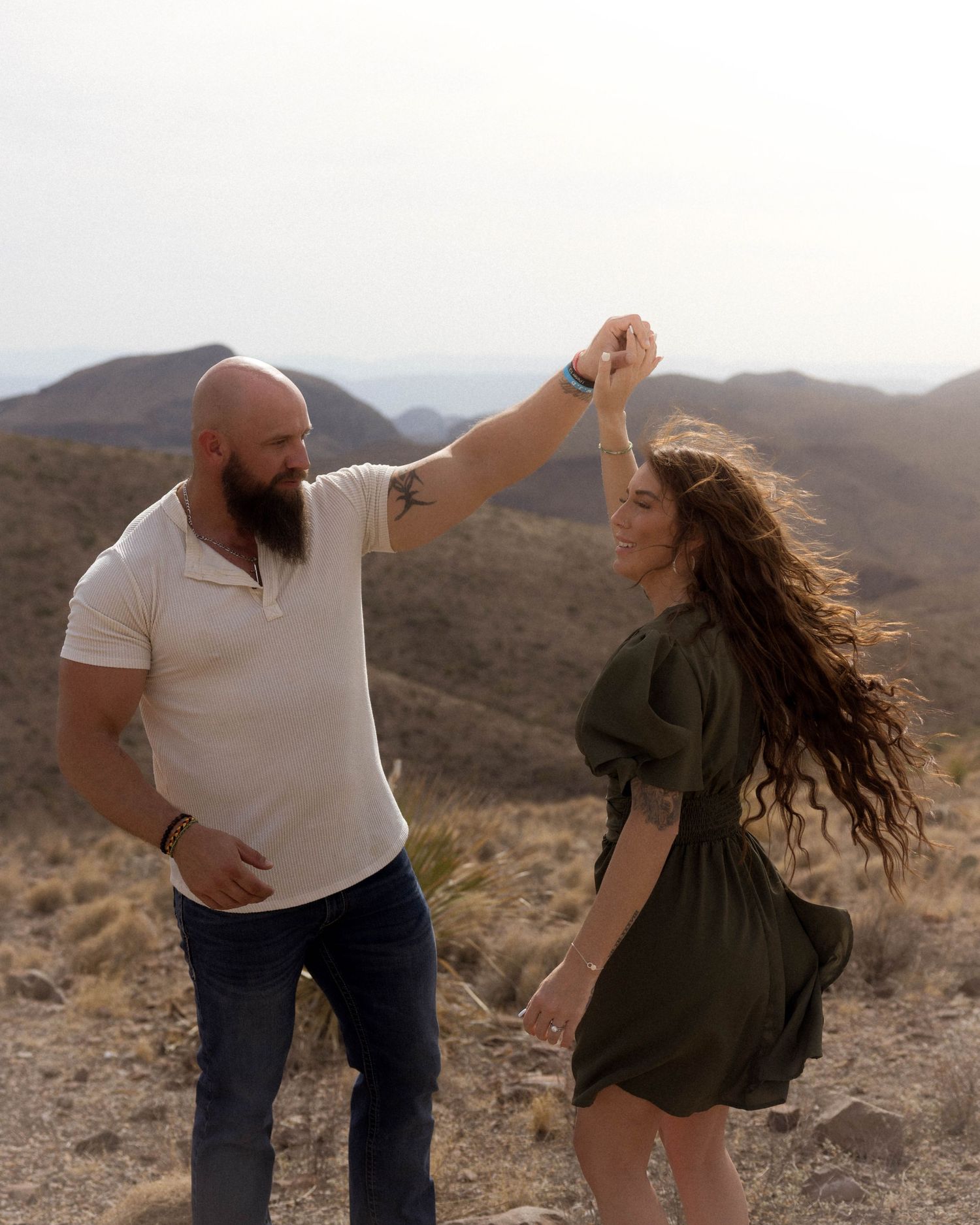 A couple dancing and twirling together against a desert mountain landscape at sunset.