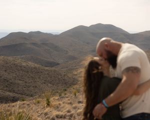 A couple shares a romantic moment against the backdrop of rugged desert mountains and golden light.