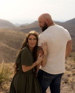 A couple embraces while posing in front of desert mountains during a romantic photoshoot.