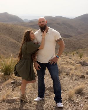 A playful couple poses together in a desert landscape with mountains and desert plants in the background.
