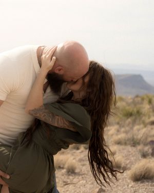A romantic couple embracing and sharing an intimate moment in a desert setting with mountains in background.